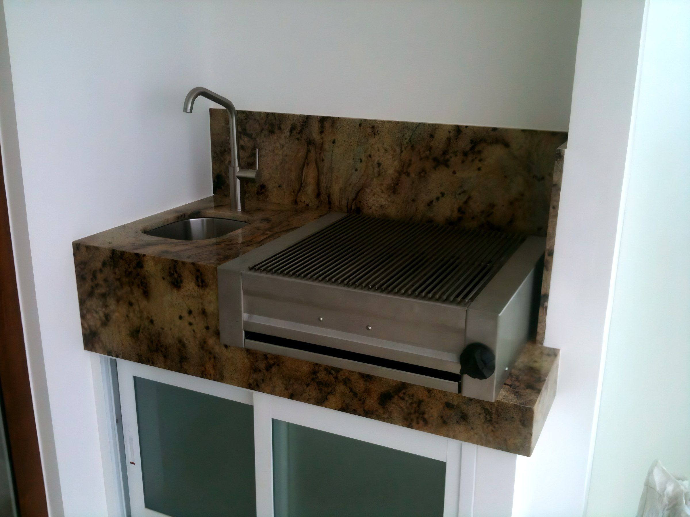 Asador de acero inoxidable empotrado en cubierta de granito, junto a una tarja.