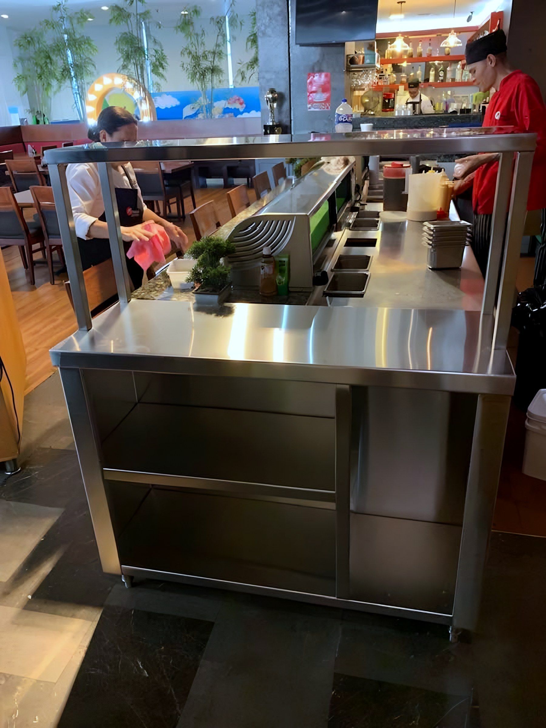 Mesa de servicio con repisa superior y entrepaños en la barra de un restaurante.