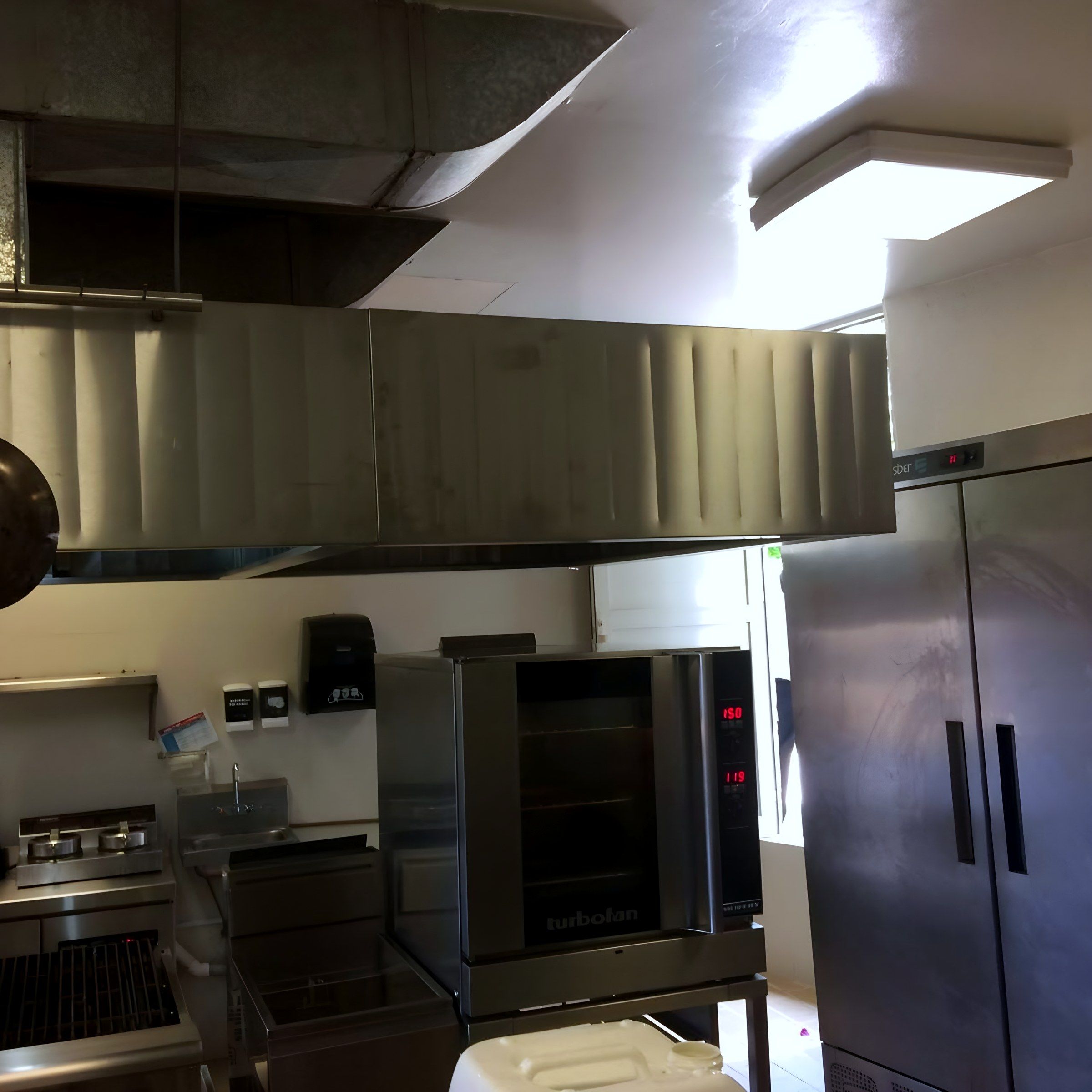 Campana de extracción sobre horno de convección, freidora y asador, junto a un refrigerador de dos puertas.
