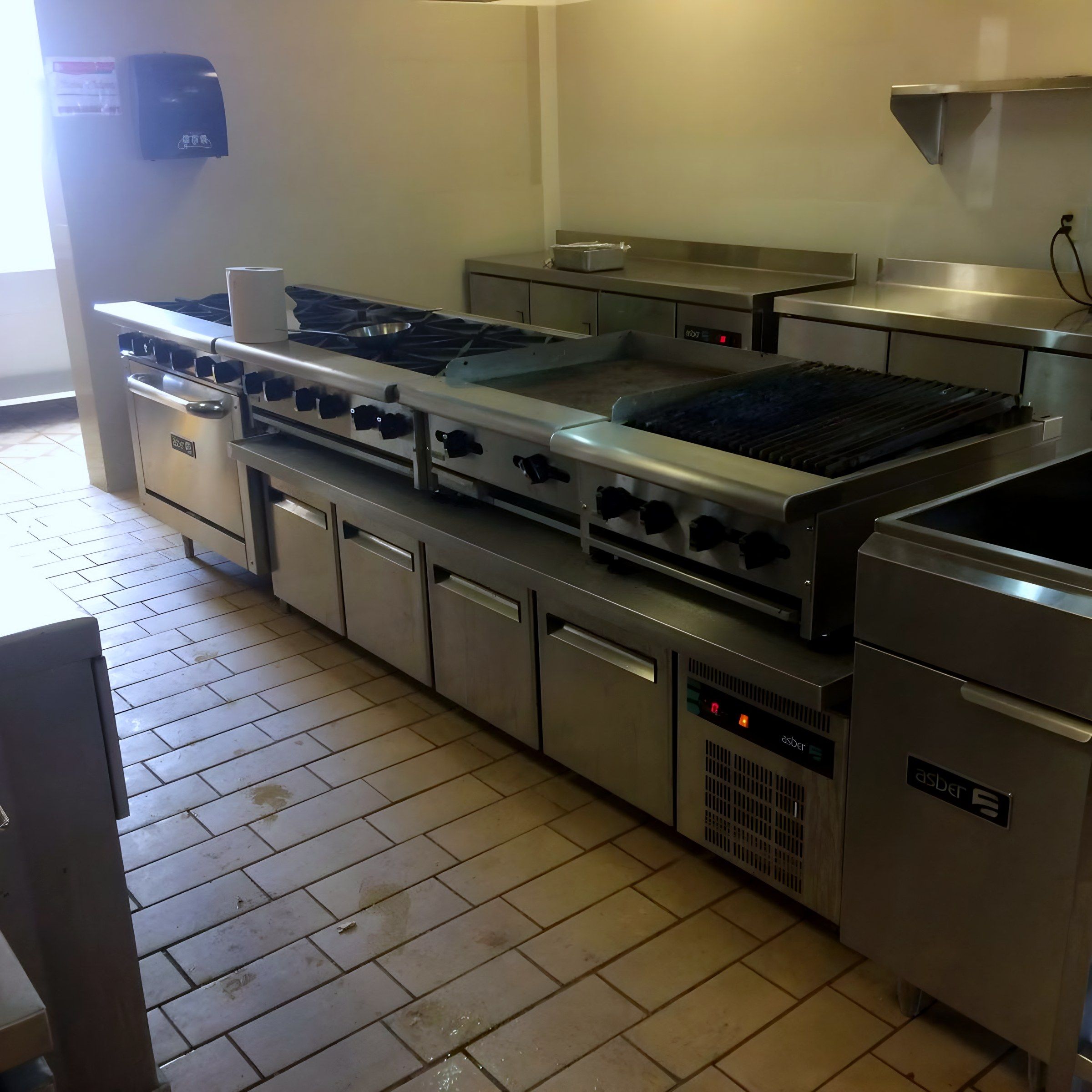 Línea de cocción con estufas, plancha y asador sobre bases refrigeradas.