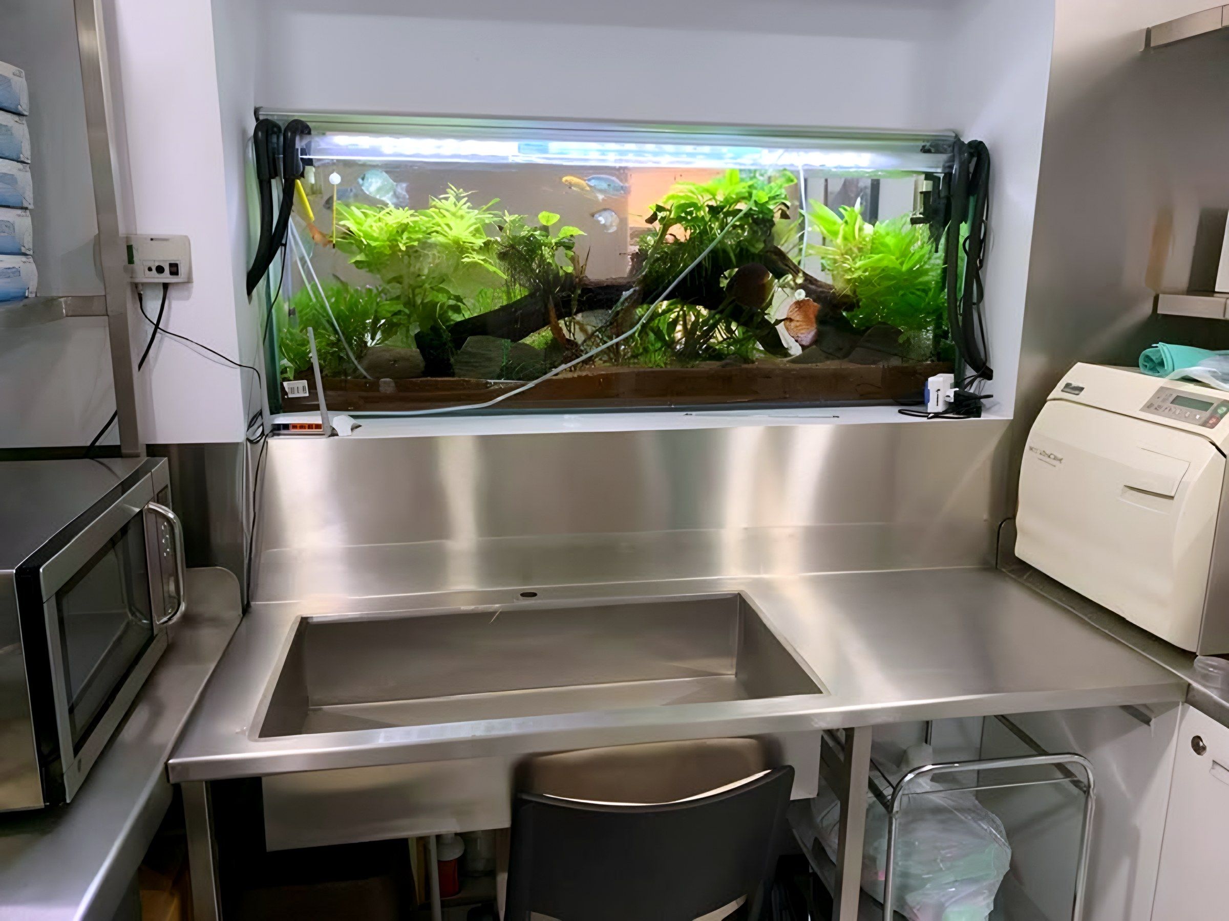 Mesa con tarja y respaldo alto en acero inoxidable, bajo un acuario empotrado.